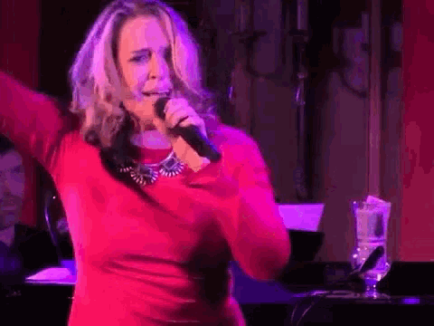 a woman in a red dress is singing into a microphone while standing on a stage .