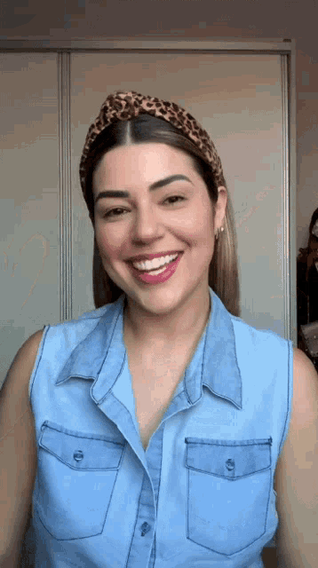a woman wearing a denim shirt and a leopard print headband smiles for the camera