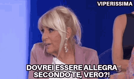 a woman is sitting in front of a blue wall and saying dovrei essere allegra secondo te vero .