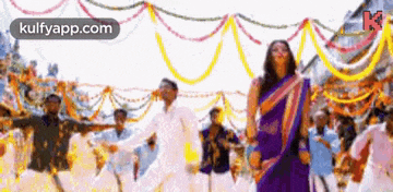 a woman in a purple sari is dancing with a group of people in a crowd .