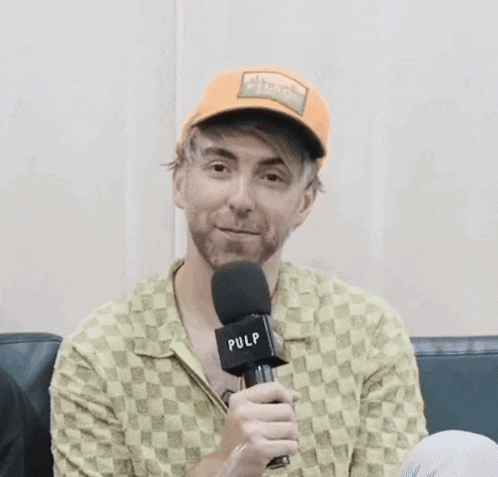 a man with a beard is holding a microphone while wearing an orange hat .