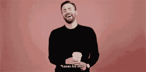 a man with a beard is laughing while holding a cup of coffee and saying `` loses his shit '' .