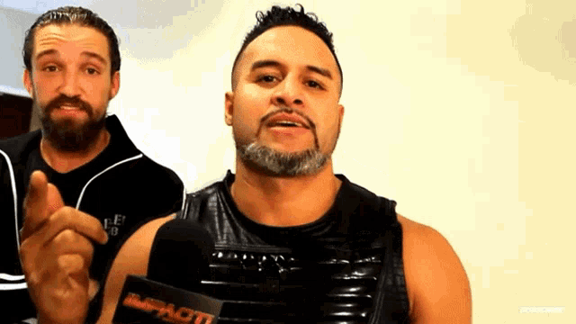 two men are standing next to each other and one of them is wearing a vest that says impact