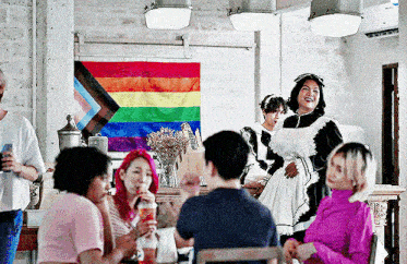 a group of people are gathered around a table with a rainbow flag in the background