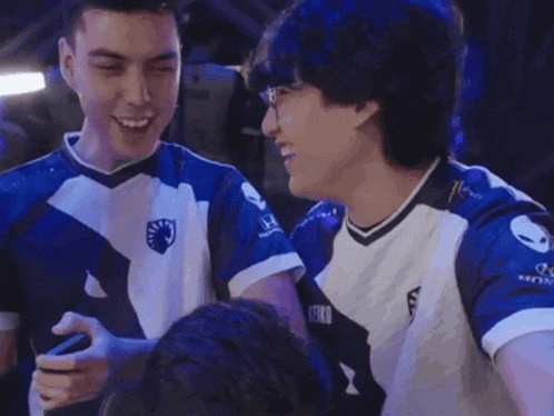 two men in blue and white jerseys are laughing while looking at a cell phone .