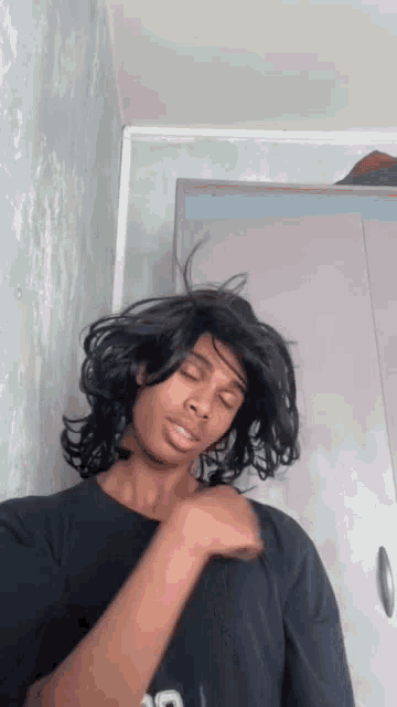 a young man with long hair is wearing a black shirt and making a funny face