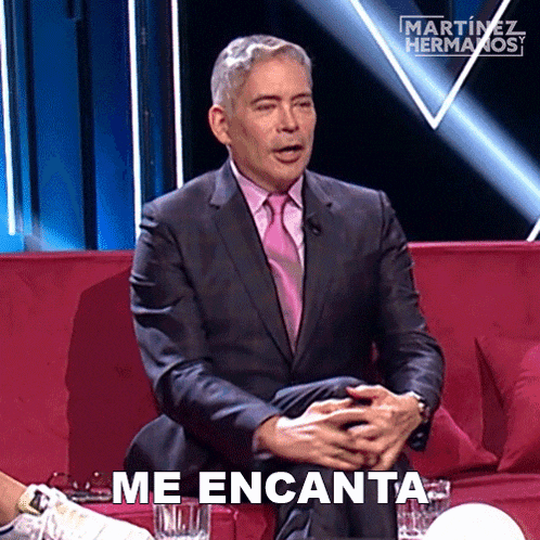 a man in a suit and tie is sitting on a red couch with the words me encanta behind him