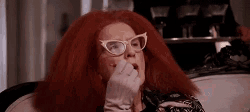 a woman with red hair and glasses is sitting on a couch and eating something .
