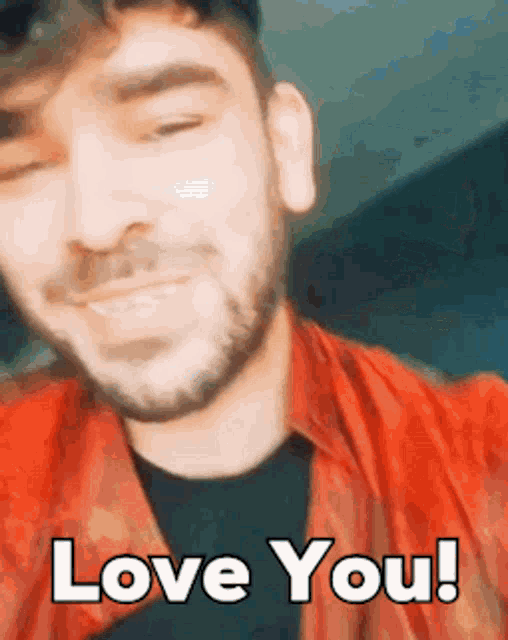a man with a beard wearing a red shirt is smiling and saying i love you !