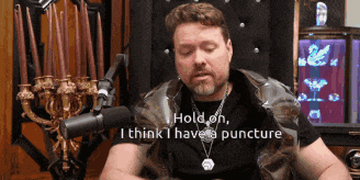 a man sitting in front of a microphone with the words " hold on i think i have a puncture "