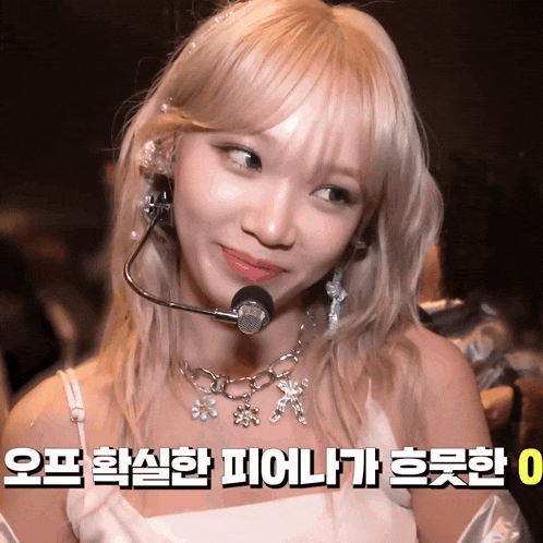a blonde woman wearing a microphone and a necklace with flowers on it