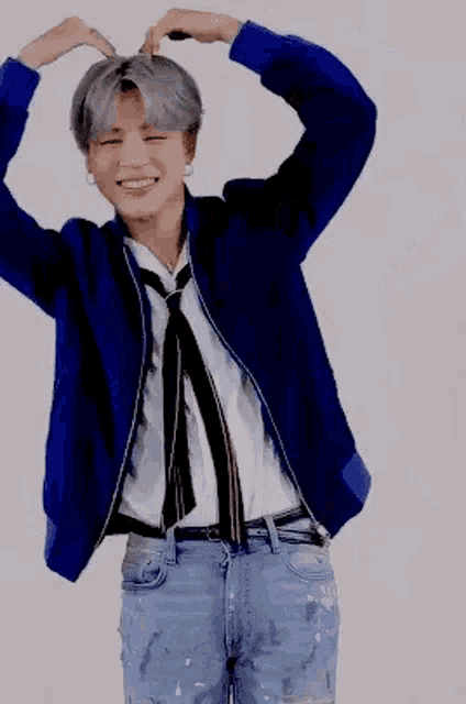 a man wearing a blue jacket and tie is making a heart with his hands .