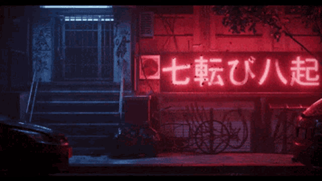 a neon sign that says ' 七転び八起 ' is lit up in red