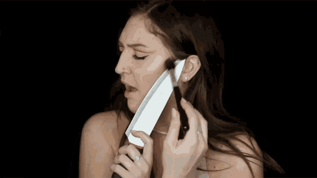 a woman is singing into a microphone while holding a large knife in front of her mouth .