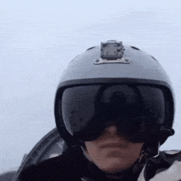a person wearing a helmet and goggles is standing in front of a cloudy sky .