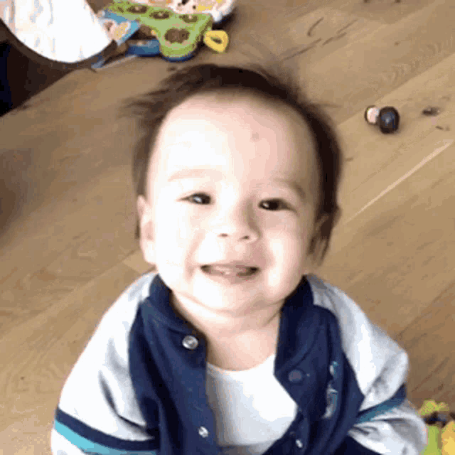 a baby is sitting on a wooden table and smiling at the camera .
