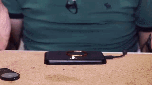 a man in a green shirt is sitting at a table with a cell phone on top of it .