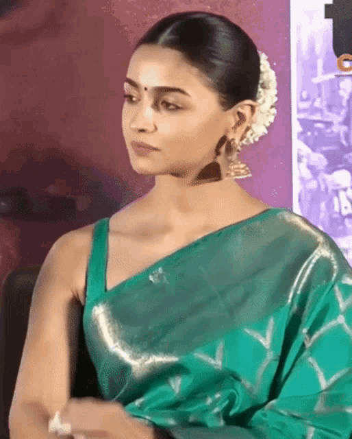 a woman in a green saree with a flower in her hair is sitting down .