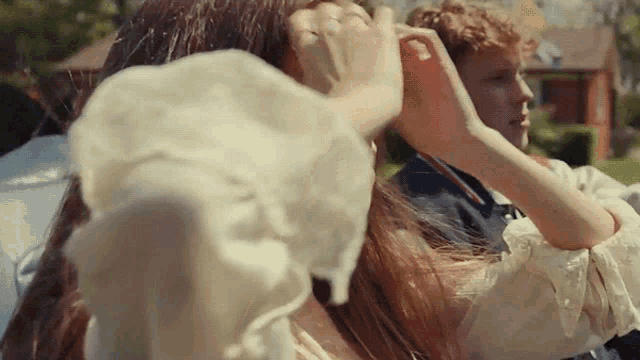 a man and a woman are sitting in a car and the woman is adjusting the man 's hair .