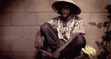 a man wearing a hat is sitting on the ground next to a flower .