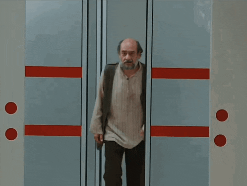 a bald man with a beard is standing in front of a door with two red circles on it