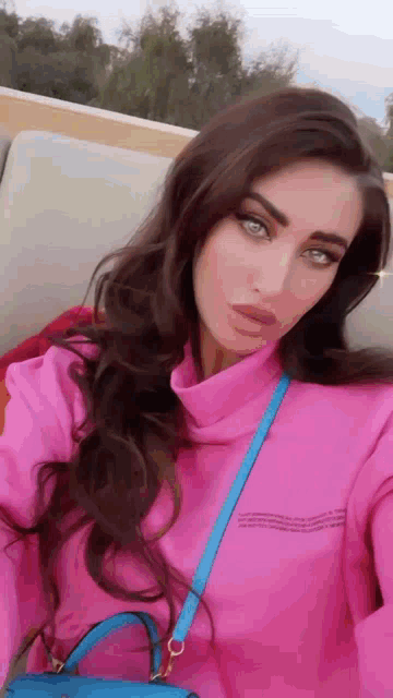 a woman in a pink sweater is taking a selfie with a blue purse