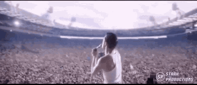 a man in a white tank top is singing into a microphone in front of a crowd .