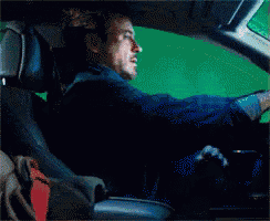 a man is sitting in the driver 's seat of a car with a green screen behind him .