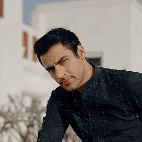 a man wearing a black shirt with embroidery on the sleeves looks at the camera
