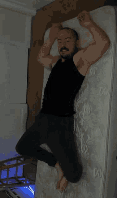 a man in a black tank top is laying on top of a mattress
