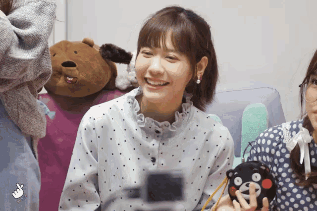 a girl in a polka dot shirt smiles while holding a stuffed bear