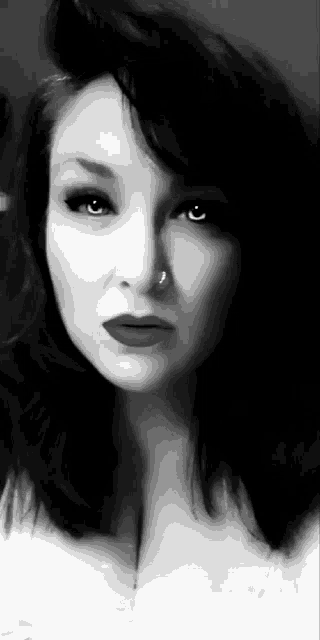 a black and white photo of a woman with a nose ring and red lipstick .