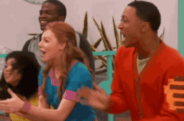 a group of people are sitting around a table and laughing . one of the people is wearing a red sweater .