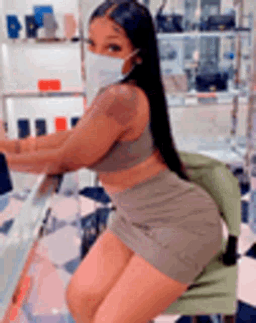 a woman wearing a mask and a crop top is sitting on a chair in a store .