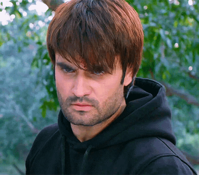 a man with a beard is wearing a black hoodie and looking at the camera