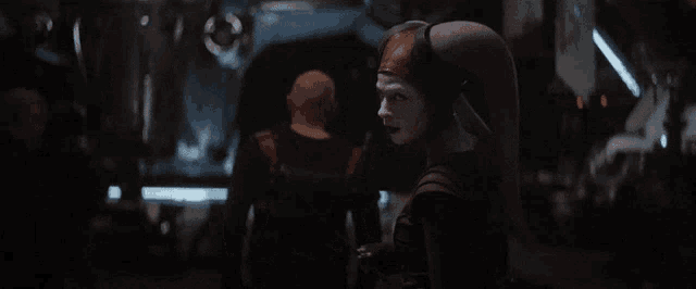 a woman in a costume is standing in a dark room with a man behind her