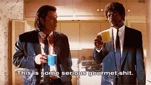 two men in suits are drinking coffee in a kitchen .