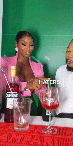 a woman in a pink top is pouring a drink into a glass that says haters on it
