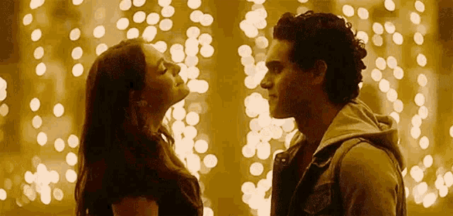 a man and woman are kissing in front of christmas lights .