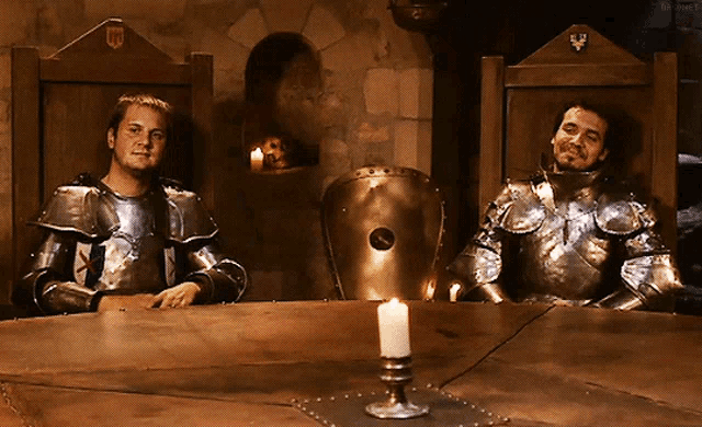 two men in armor sitting at a table with a candle