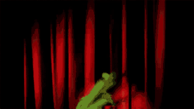 a green frog is behind a red curtain on a stage