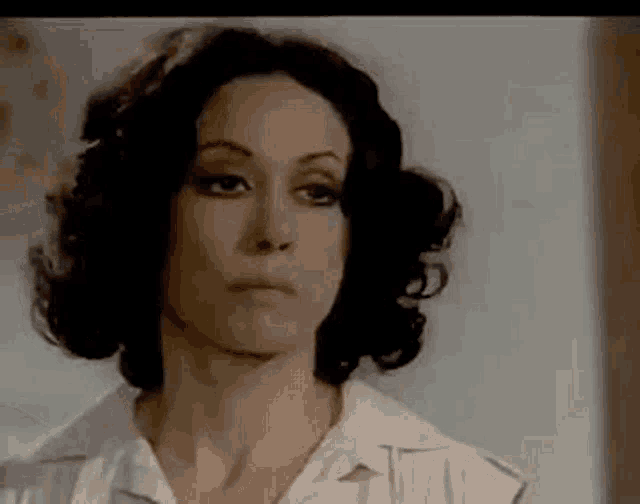 a woman with curly hair is wearing a white shirt and making a serious face .