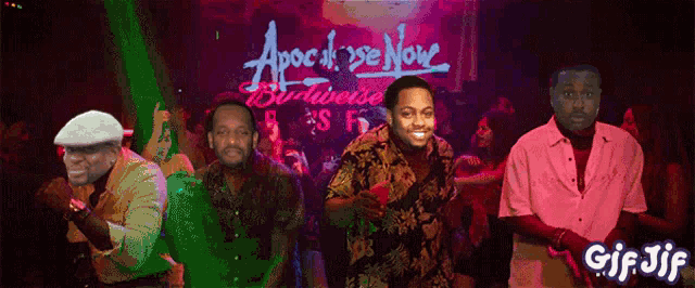 four men are dancing in front of a sign that says apocalypse now