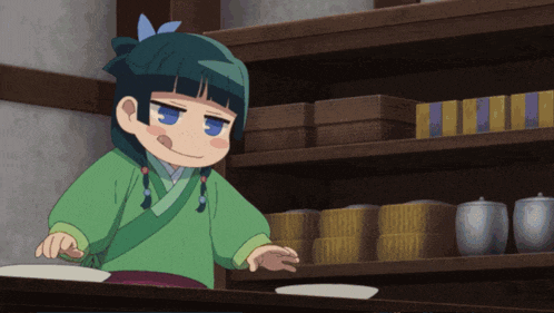 a little girl in a green outfit is standing in front of a shelf with boxes on it