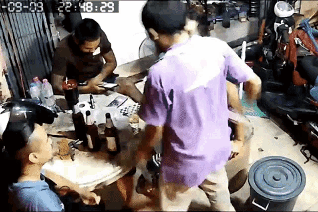 a group of men are sitting around a table with bottles of alcohol and a bucket .