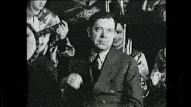 a man in a suit is standing in front of a group of people playing instruments .