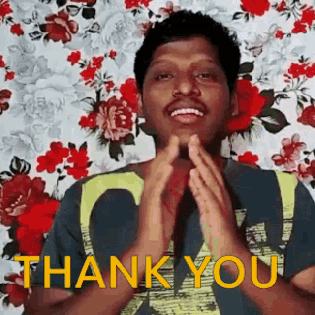 a man is smiling and clapping his hands in front of a floral background .