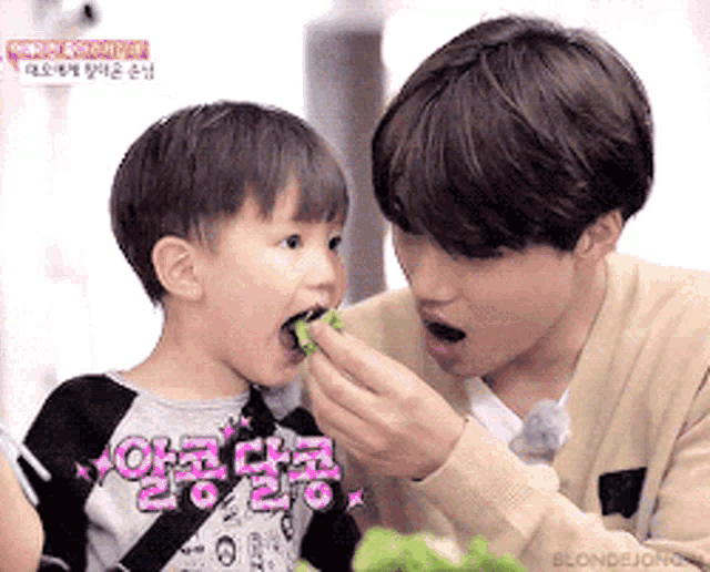 a man is feeding a little boy a piece of food while the little boy looks on .