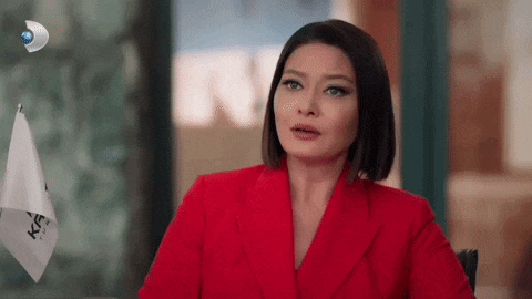 a woman in a red suit is sitting at a table and talking to someone .