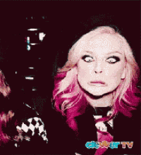 a woman with pink hair is making a funny face in front of a sign that says geek tv